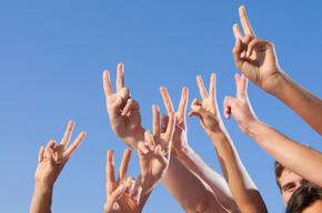 multiple hands in the air giving the peace sign