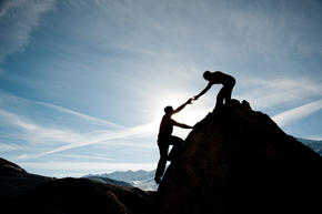 Person helping another person climb up a rock