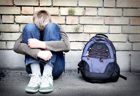 boy sitting against a wall with his head in his hands